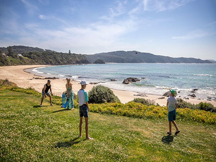 A family playing cricket on the grass below the cottage with Boat Beach in the background. Photo: