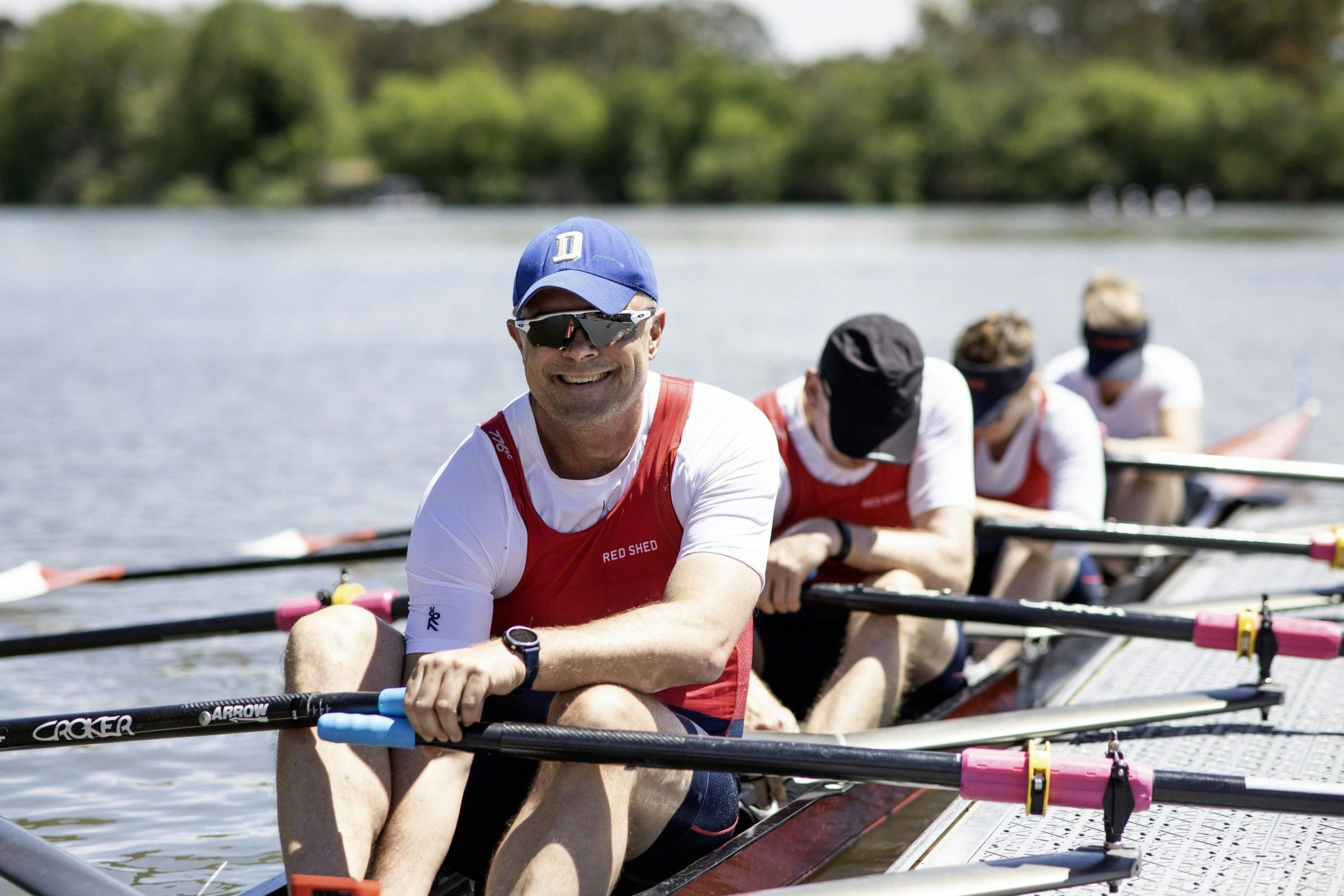Mixed quad sculling crew racing on Lake Burley Griffin with trees on the far shore