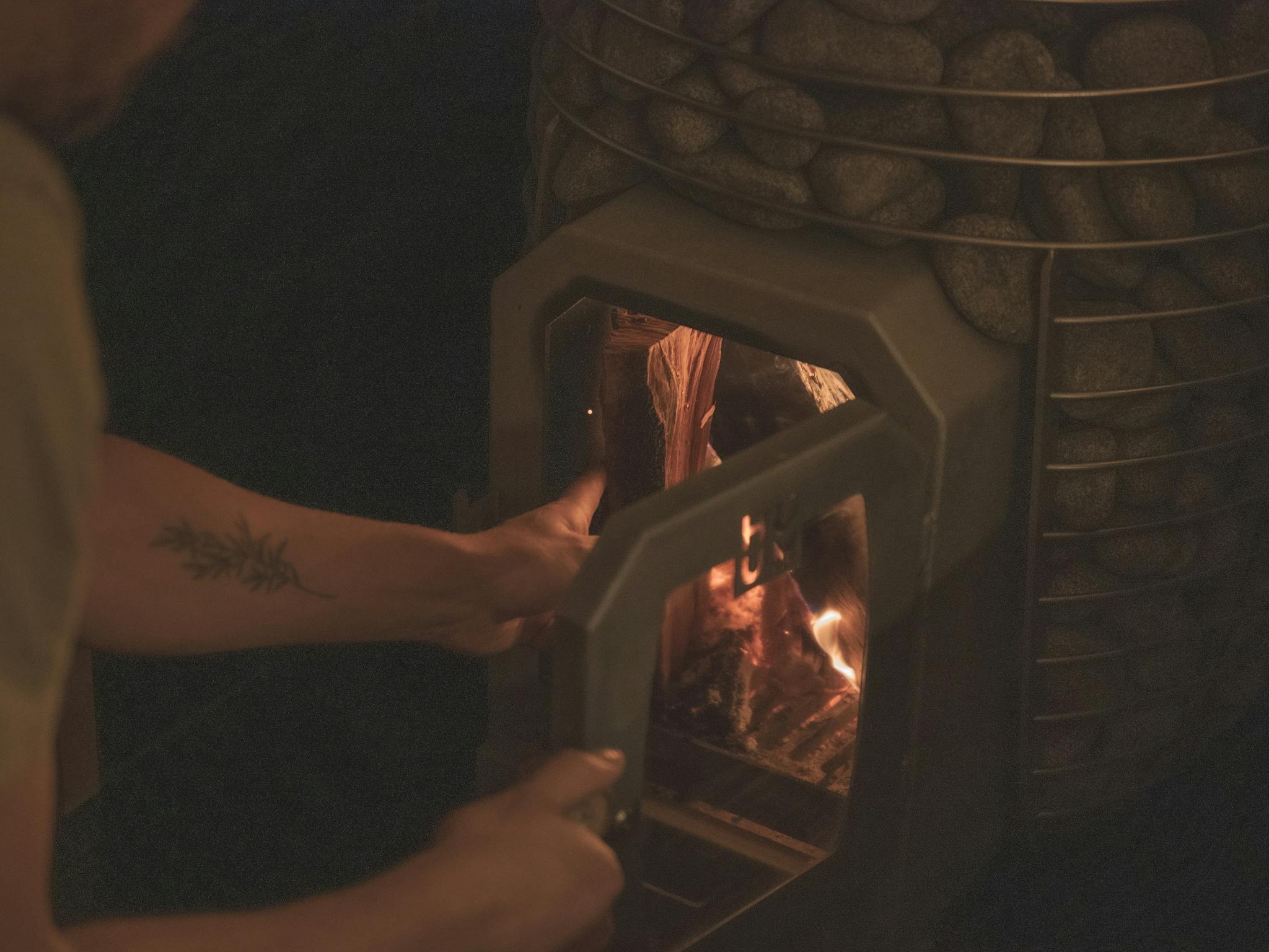 Loading wood into a wood fired Huum sauna heater in  dim lighting