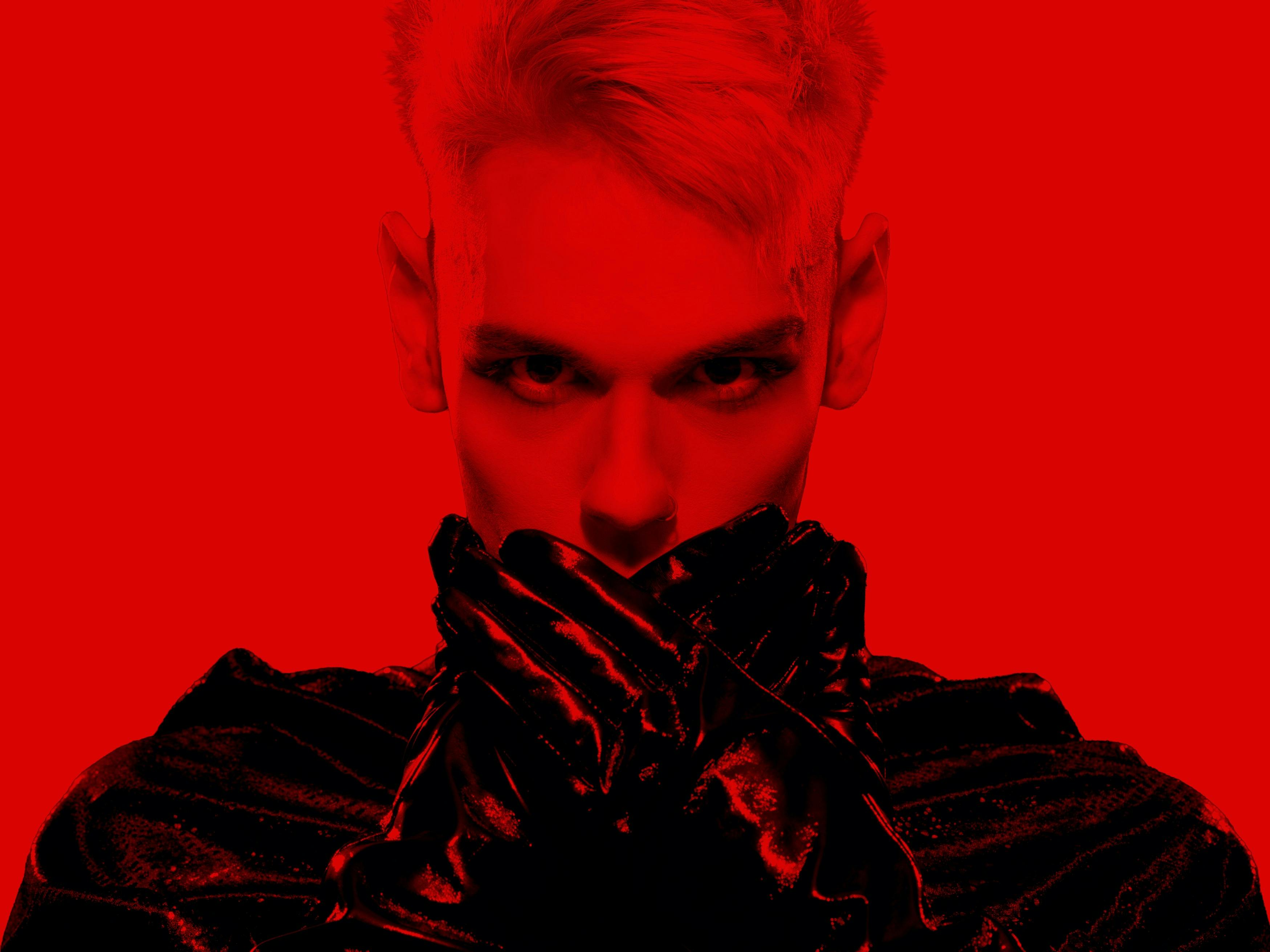 Dramatic red and black portrait of a performer staring intensely into the camera, wearing all black
