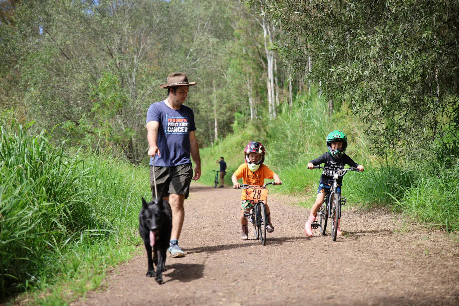 a man is walking his dog along the trail. Two young boys are riding BMX bikes next to the man.
