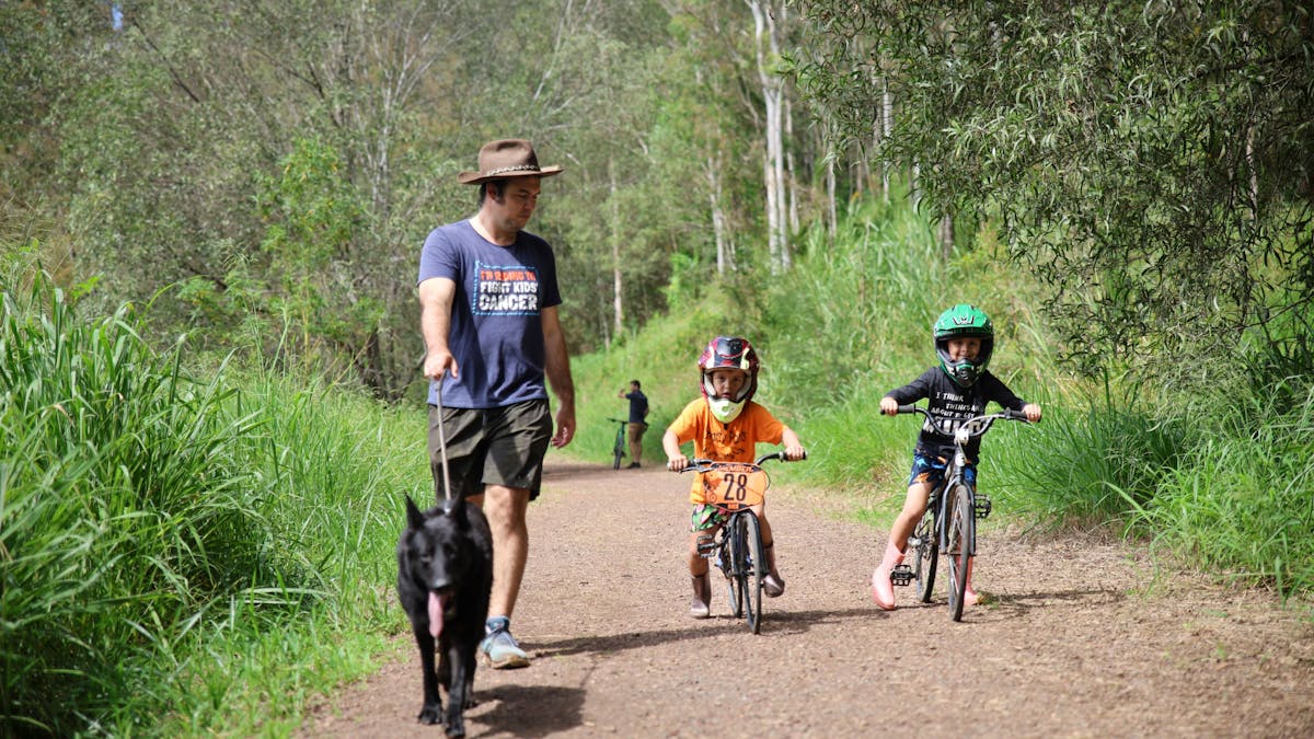 a man is walking his dog along the trail.  Two young boys are riding BMX bikes next to the man.