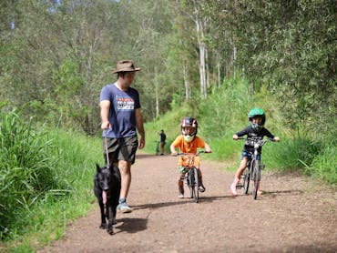 a man is walking his dog along the trail.  Two young boys are riding BMX bikes next to the man.