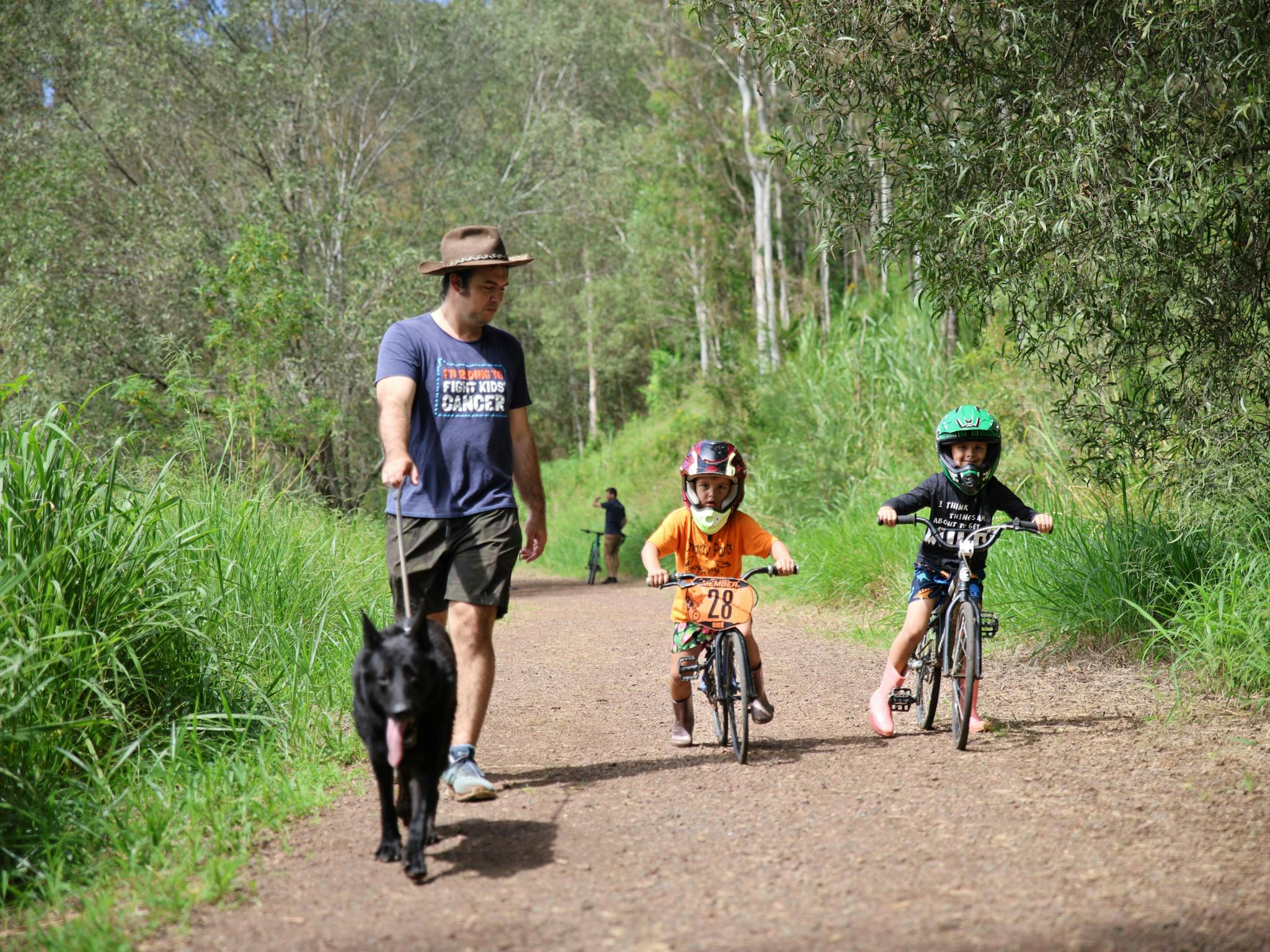 a man is walking his dog along the trail. Two young boys are riding BMX bikes next to the man. a man is walking his dog along the trail. Two young boys are riding BMX bikes next to the man.