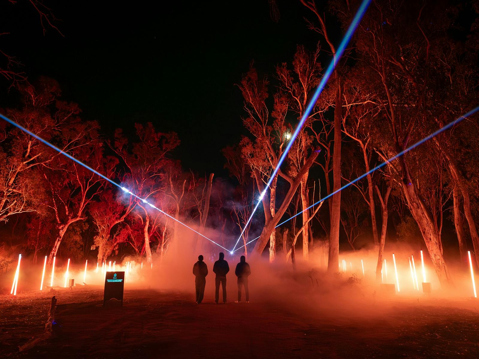 The installation is enveloped by amber fog while a blue laser pierces the sky