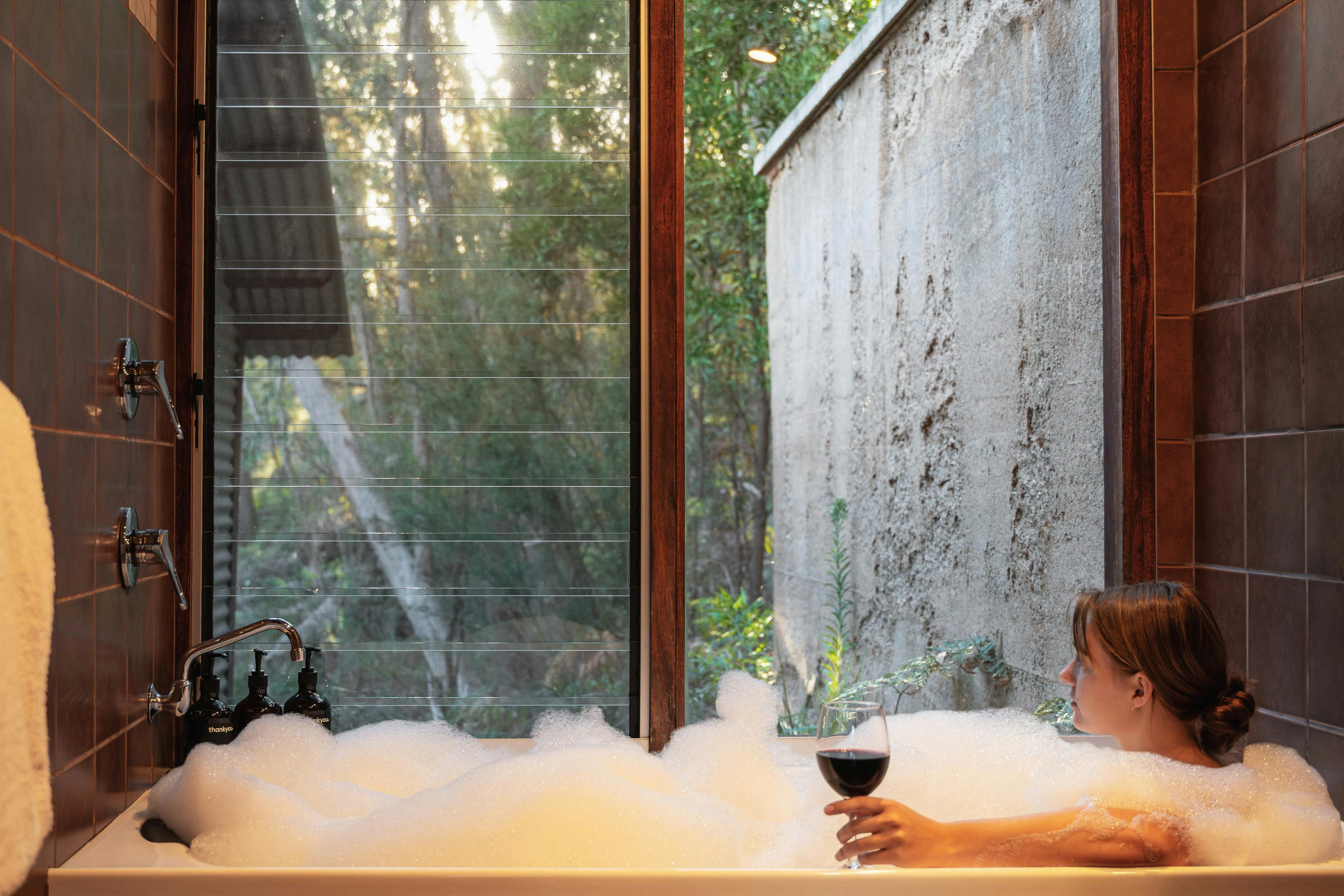 Person relaxing in the spa bath holding a glass of wine and peaceful bush views at The Odd Frog