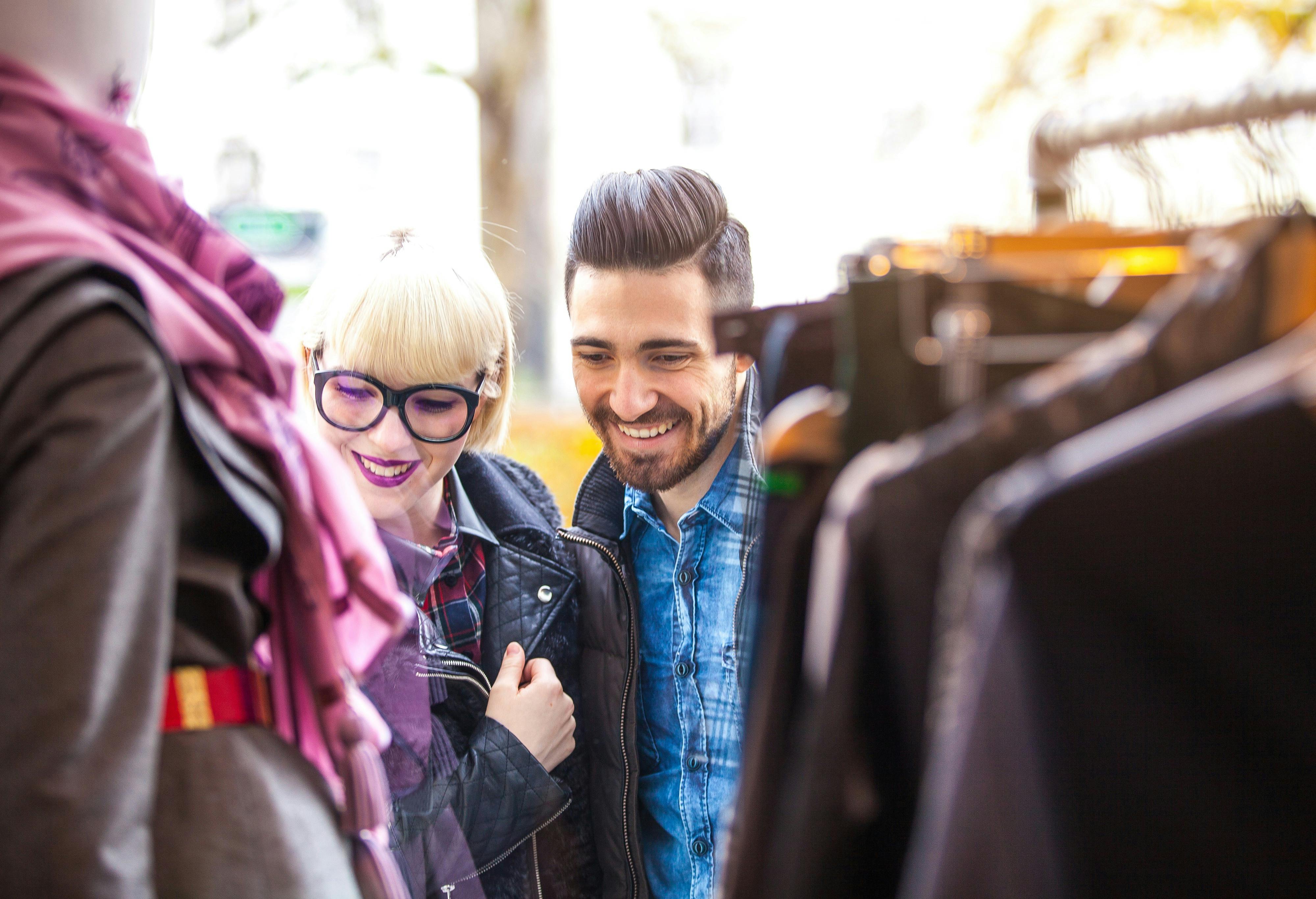 lady and a man smiling at clothing hanging up at an outdoor market