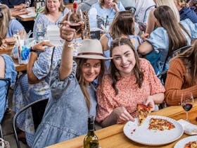 Two ladies eating pizza, cheersing their glasses and having fun