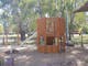 Childrens playground, wooden structure with steps to slide, leafy gum trees, shade sails