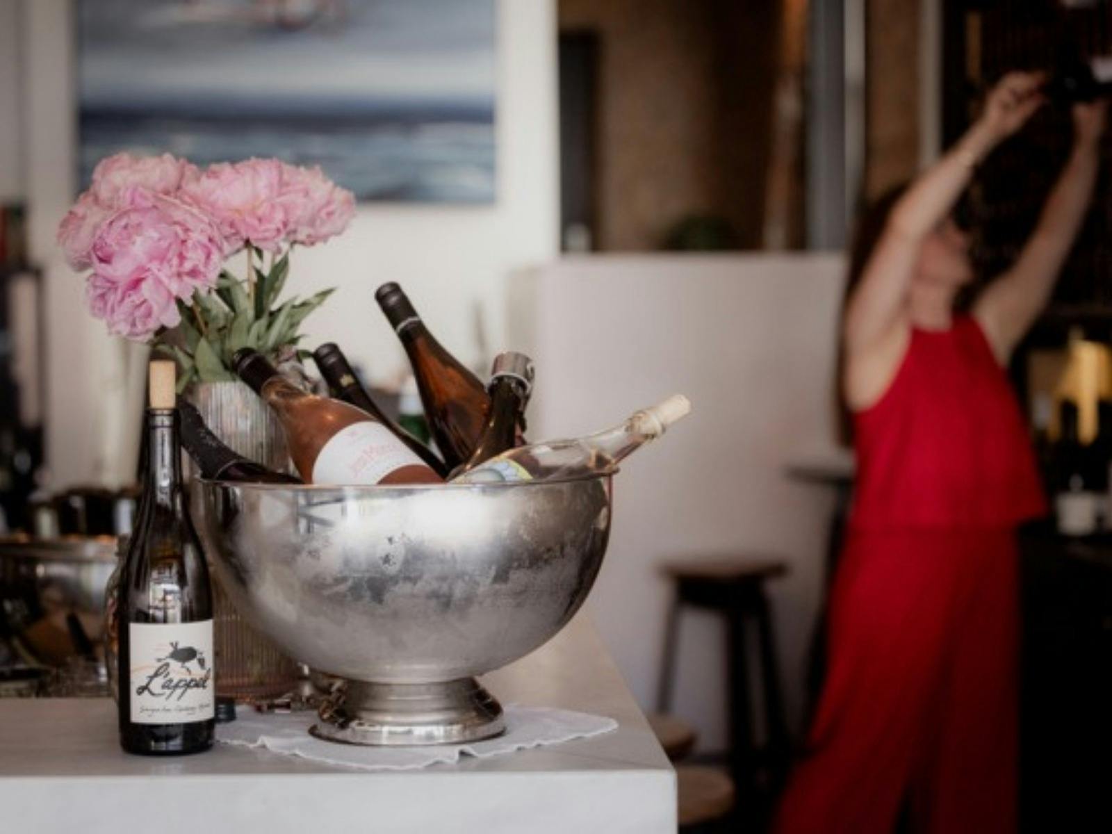 Sommelier reaching for wine with cold wine on ice in the forground on the bar with fresh peonies