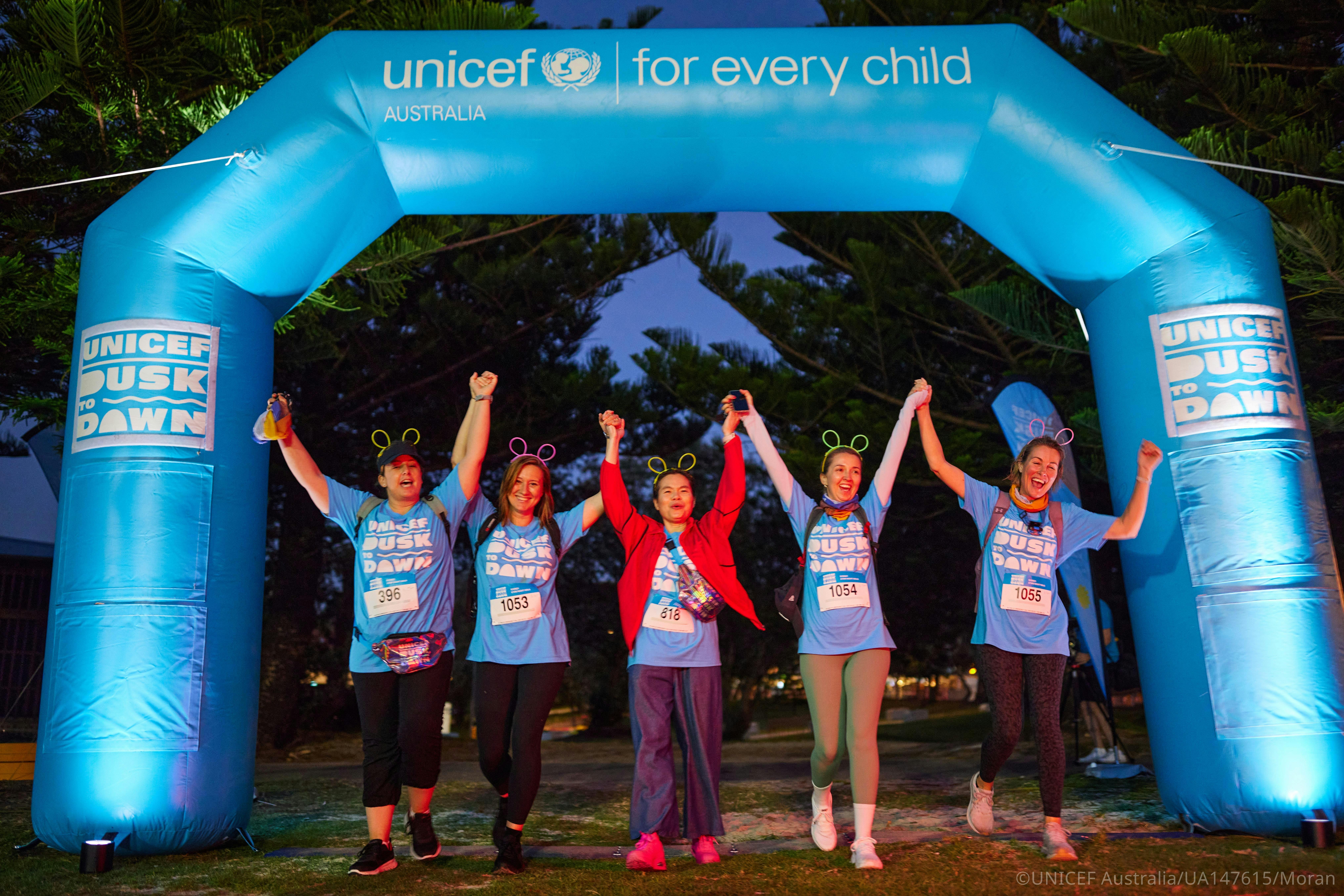 Group of Dusk to Dawn participants standing together beneath the event arch at night.