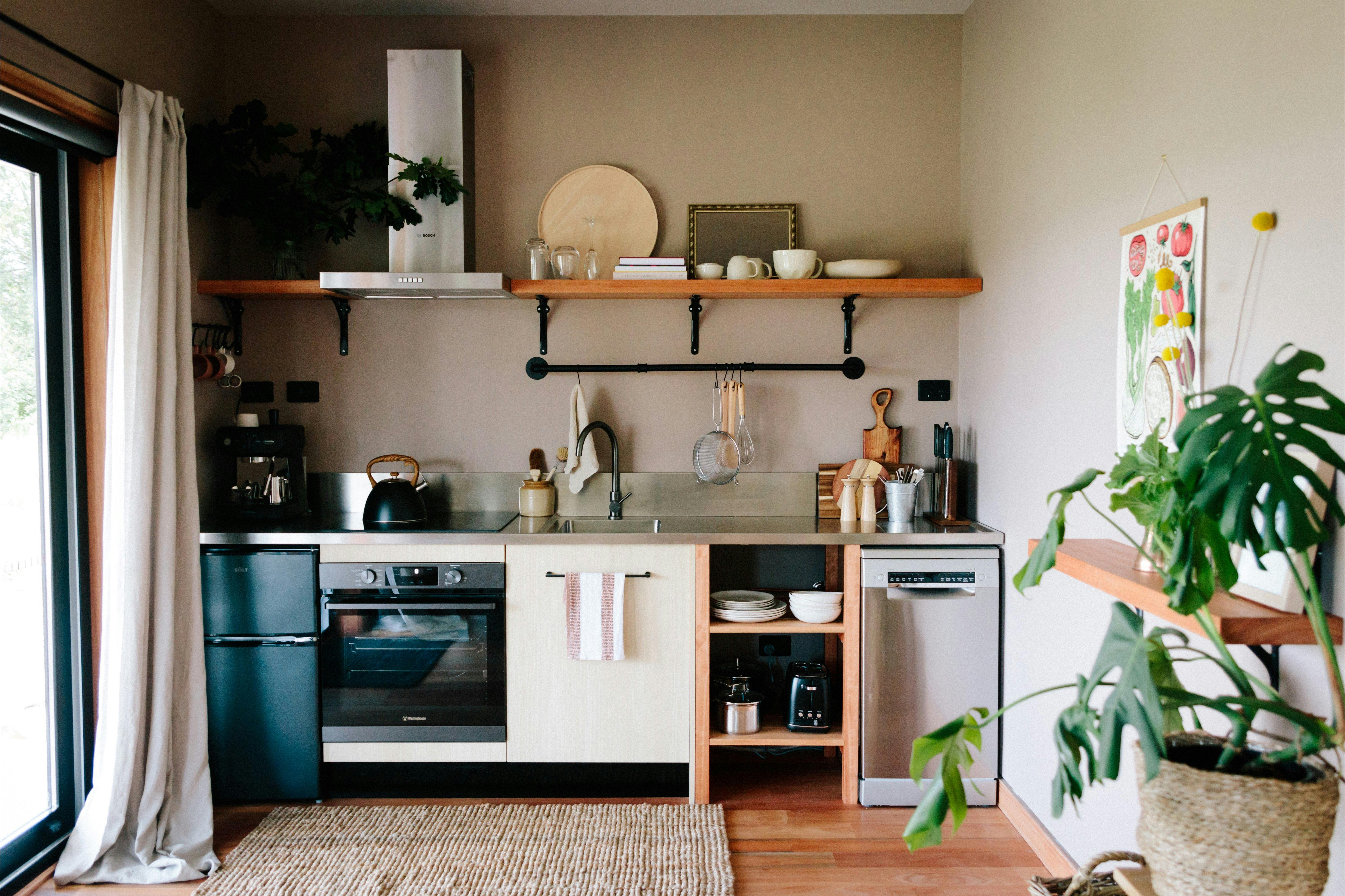A stainless steel bench with coffee maker, stovetop, kettle, sink and utensils. Appliances below.