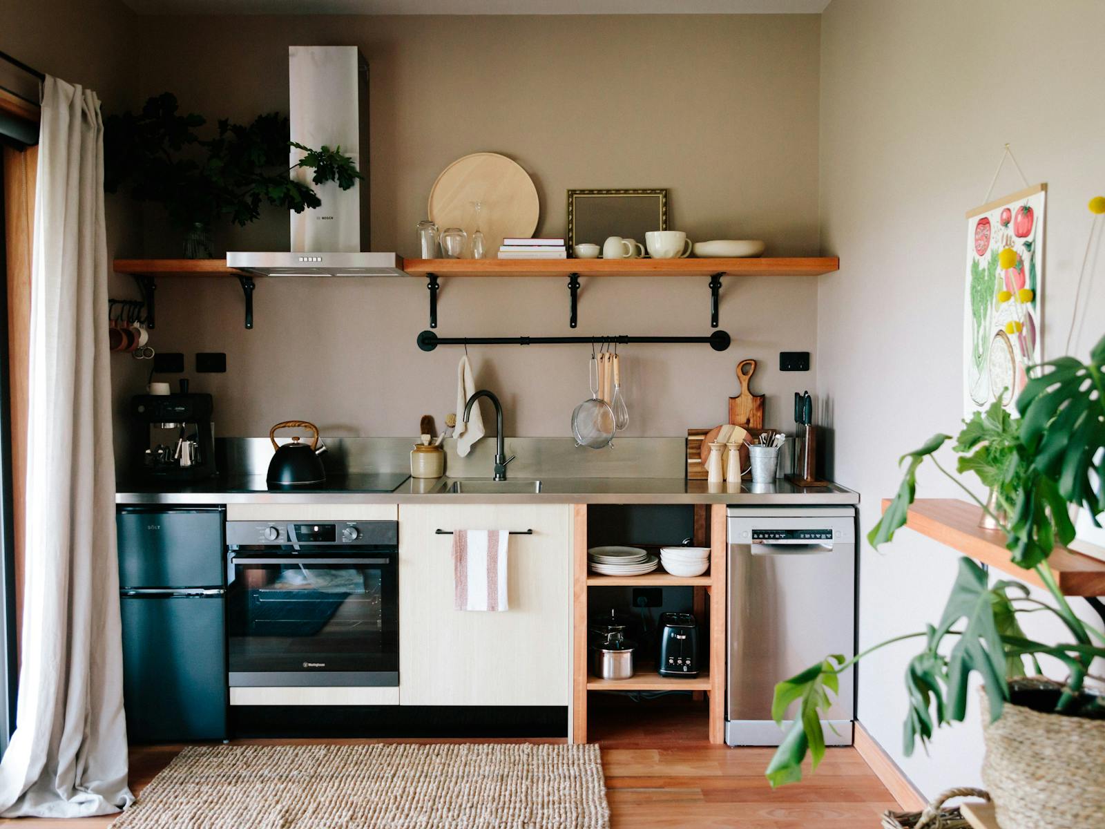 A stainless steel bench with coffee maker, stovetop, kettle, sink and utensils. Appliances below.