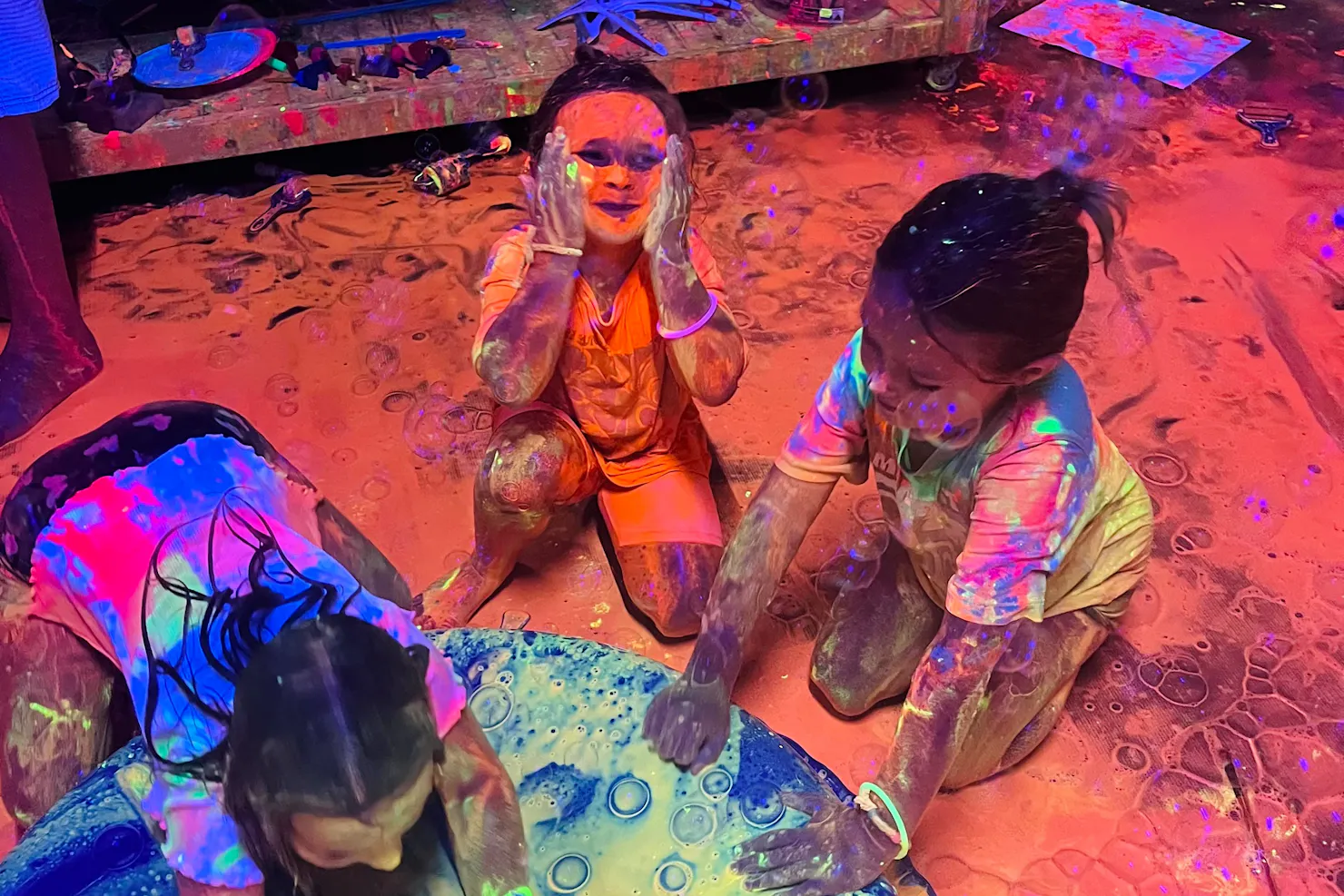 A little girl covering her face in glowing paint at Messy Glow Co UV Paint Room