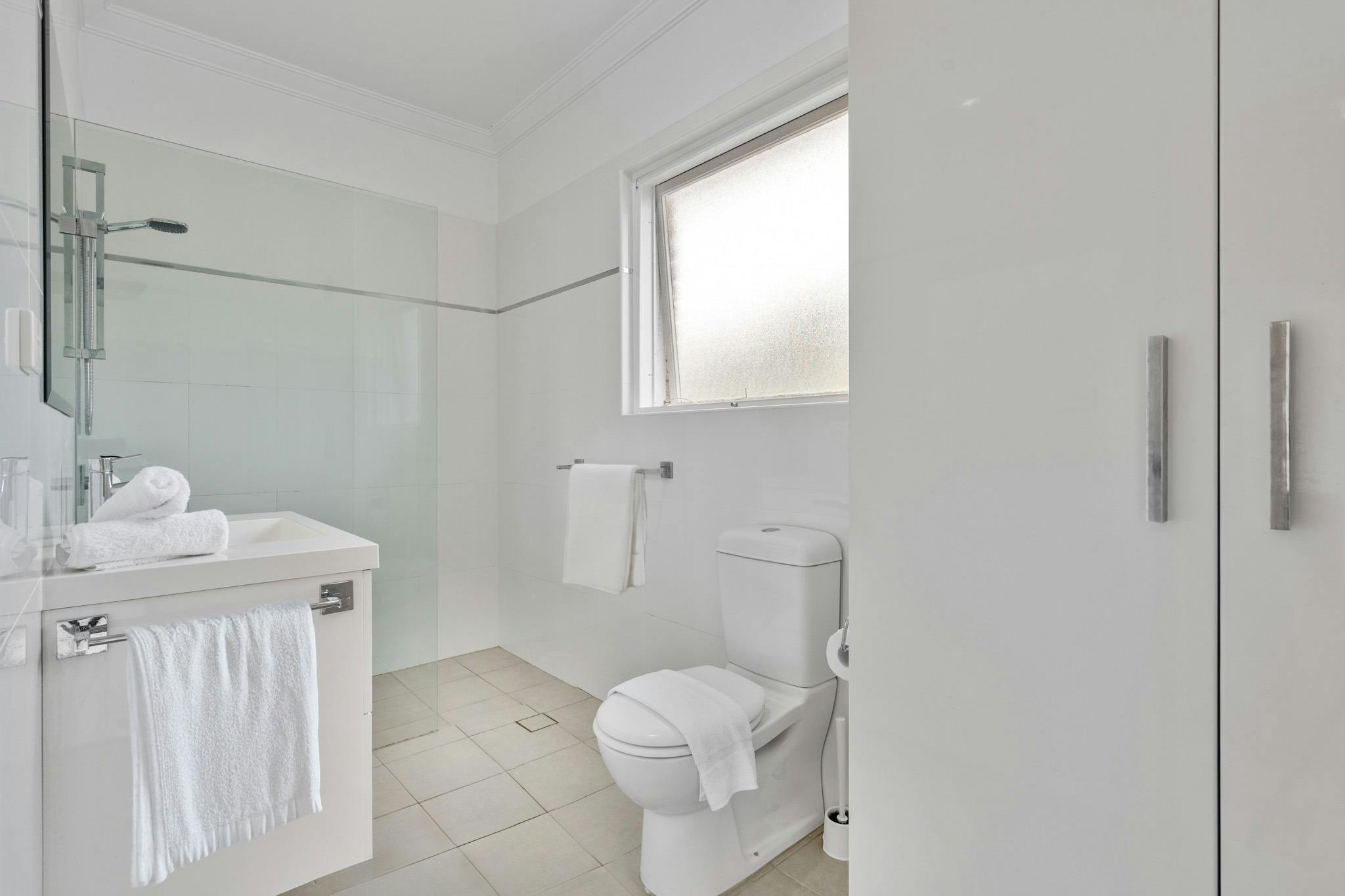 現代浴室配有步入式淋浴間、白色毛巾和簡潔的線條。