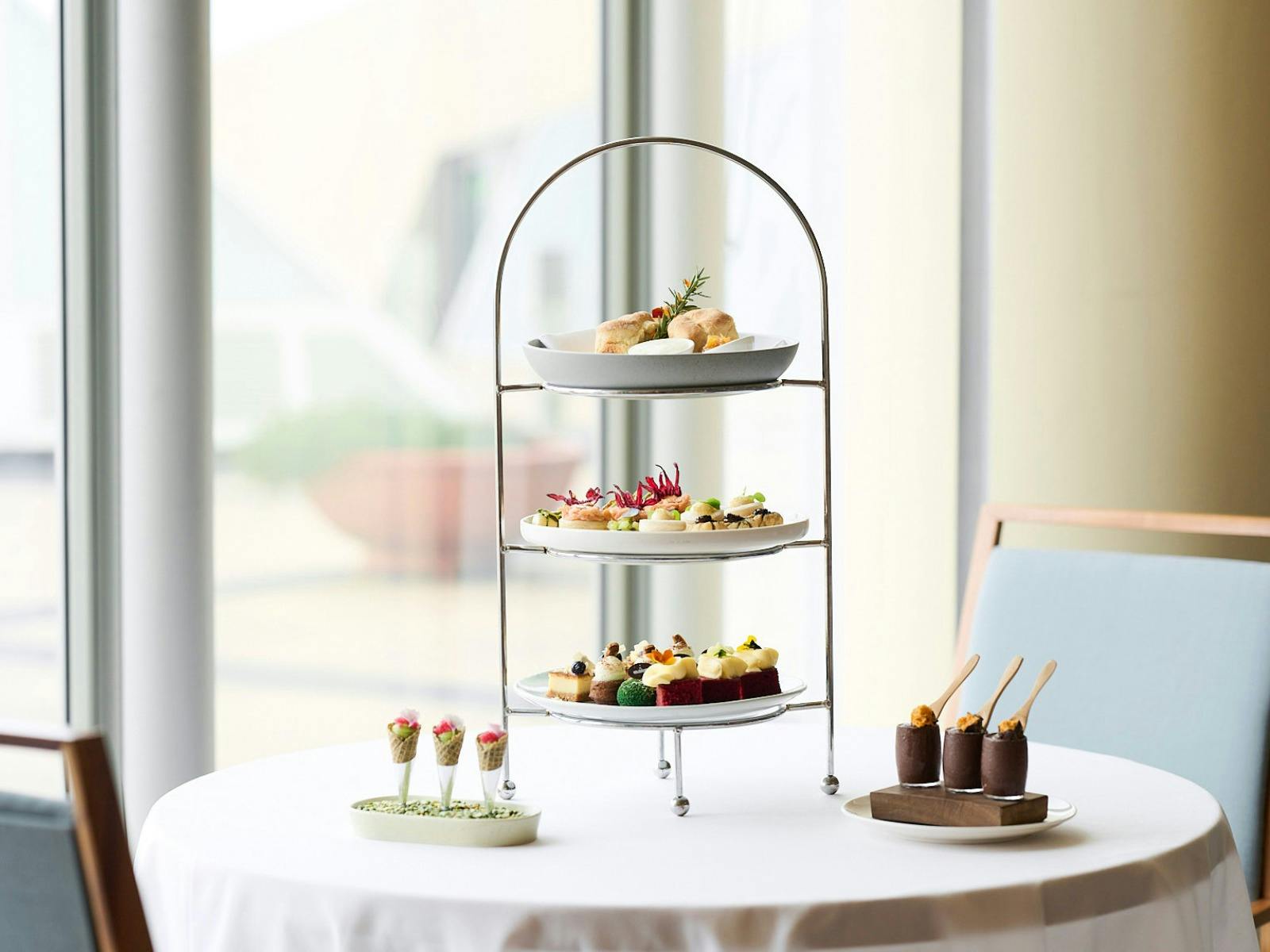 Three plates on high tea stand with two smaller dishes next to the stand.