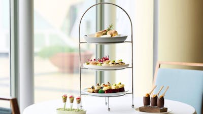 Three plates on high tea stand with two smaller dishes next to the stand.