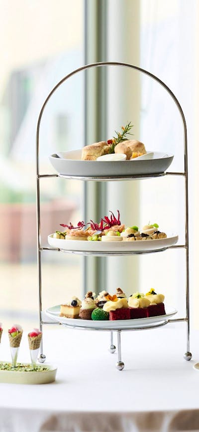 Three plates on high tea stand with two smaller dishes next to the stand.