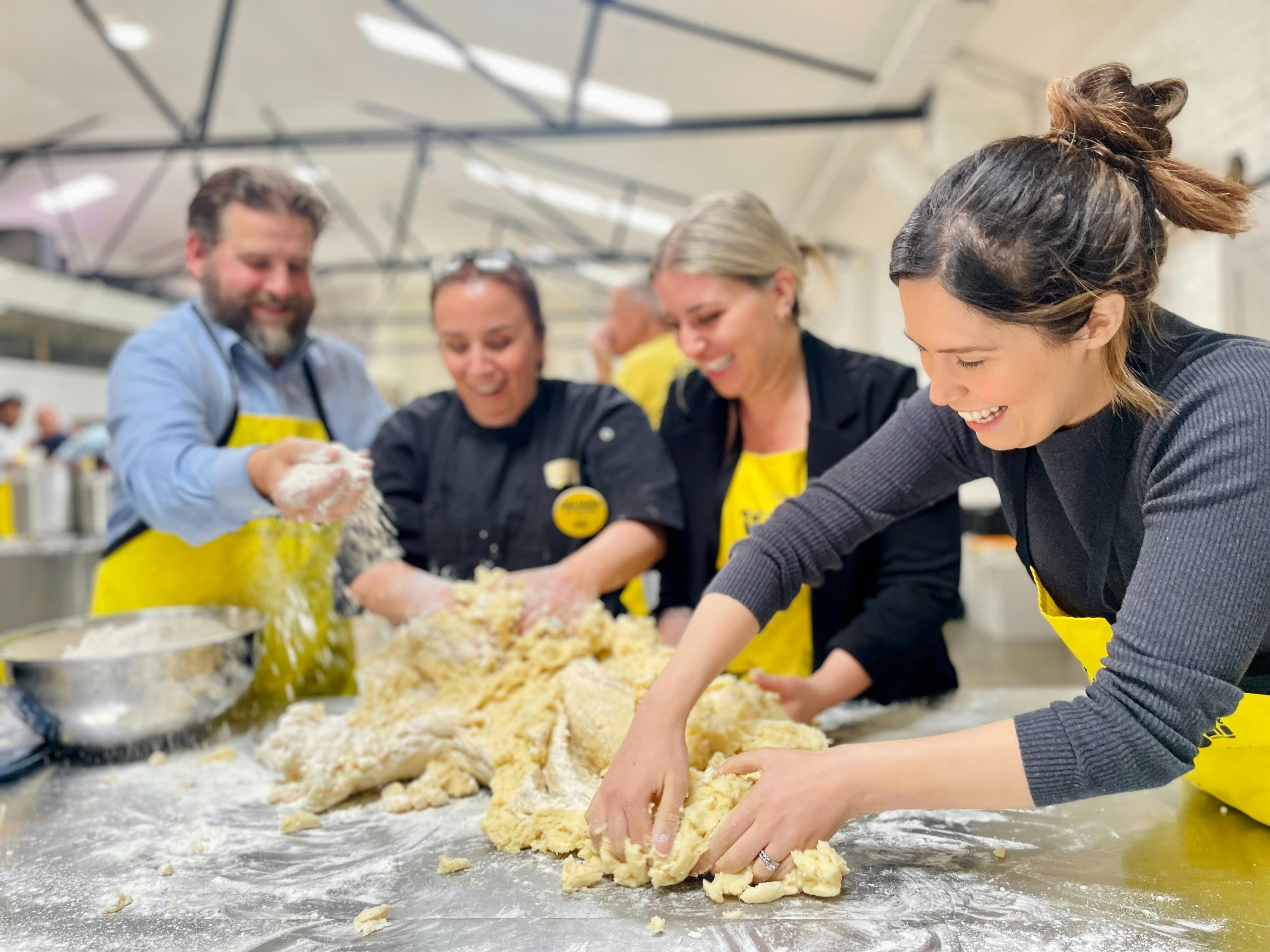 A group kneading dough together at an OzHarvest cooking class, laughing as flour scatters across the