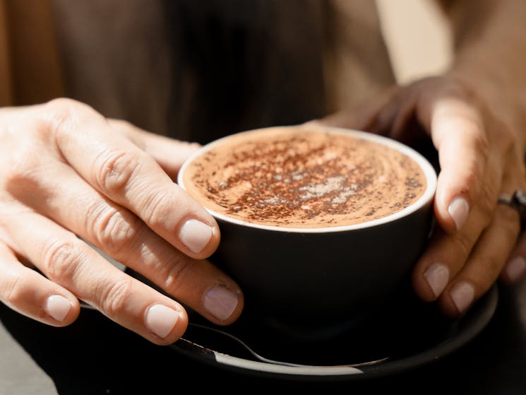 A closeup of a black cup of cappuccino being held lightly by a man's hands.