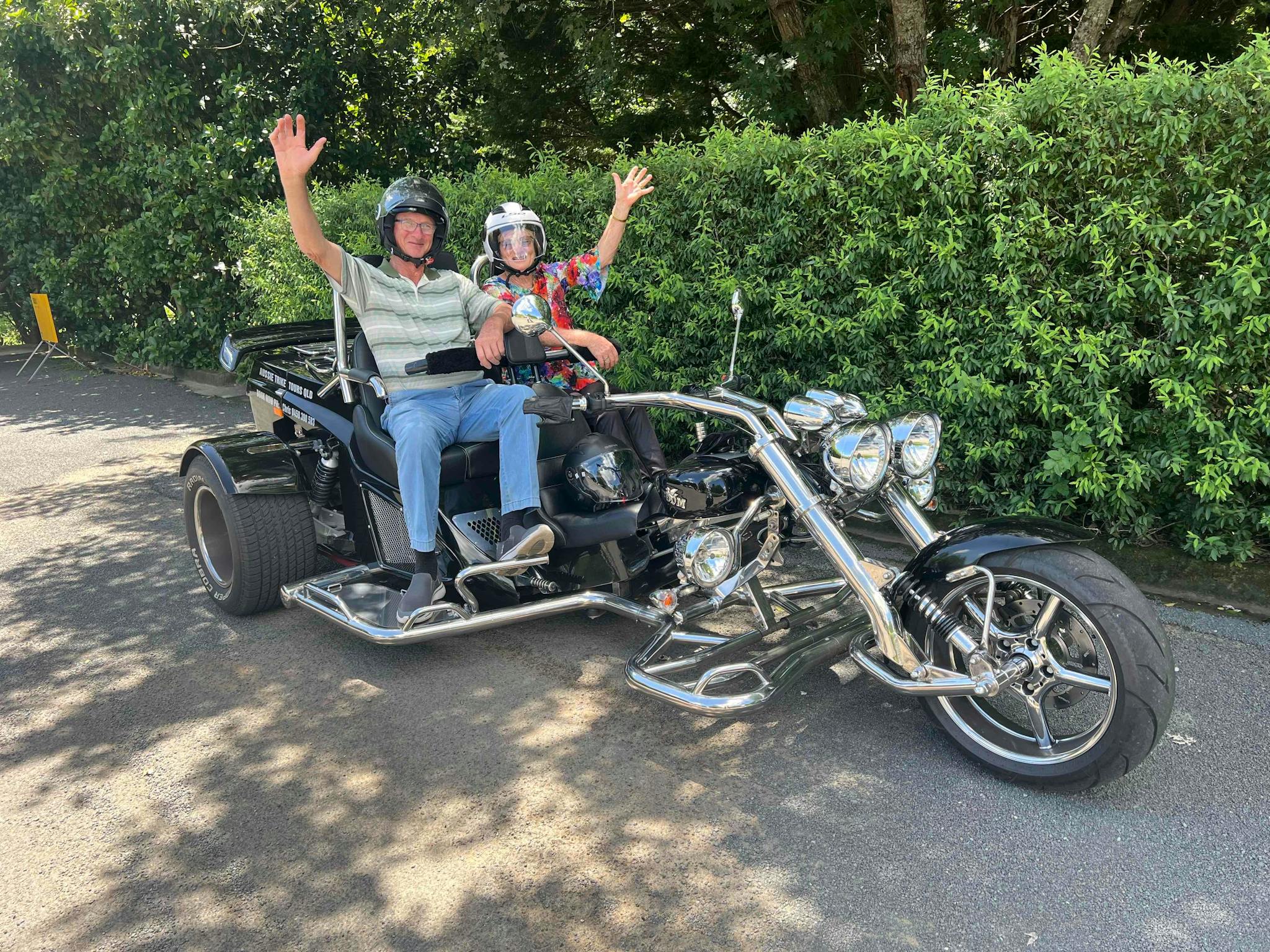 Image shows a man and a woman on the back of a trike with their hands in the air smiling. Image shows a man and a woman on the back of a trike with their hands in the air smiling.