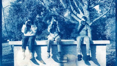 A cyanotype print photograph of three kids sitting on a ledge holding cameras up to their faces