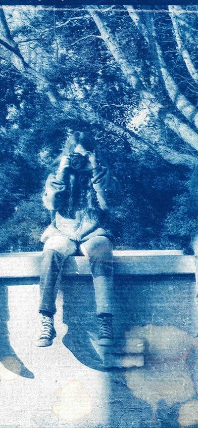 A cyanotype print photograph of three kids sitting on a ledge holding cameras up to their faces