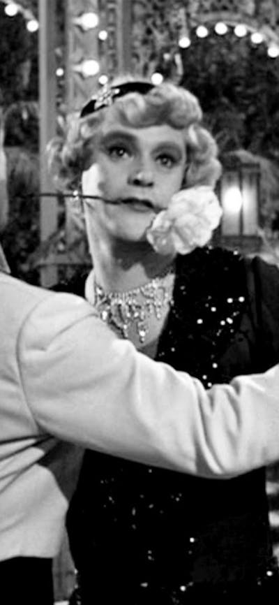 Black and white still of two men dancing, one dressed as a woman with a flower in his mouth