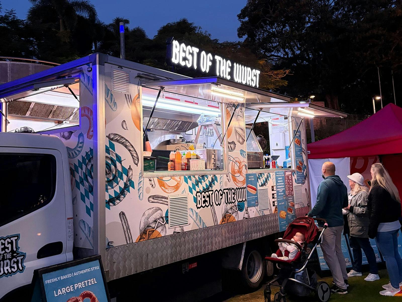 Best of the Wurst Food Truck outdoors at night with lit sign