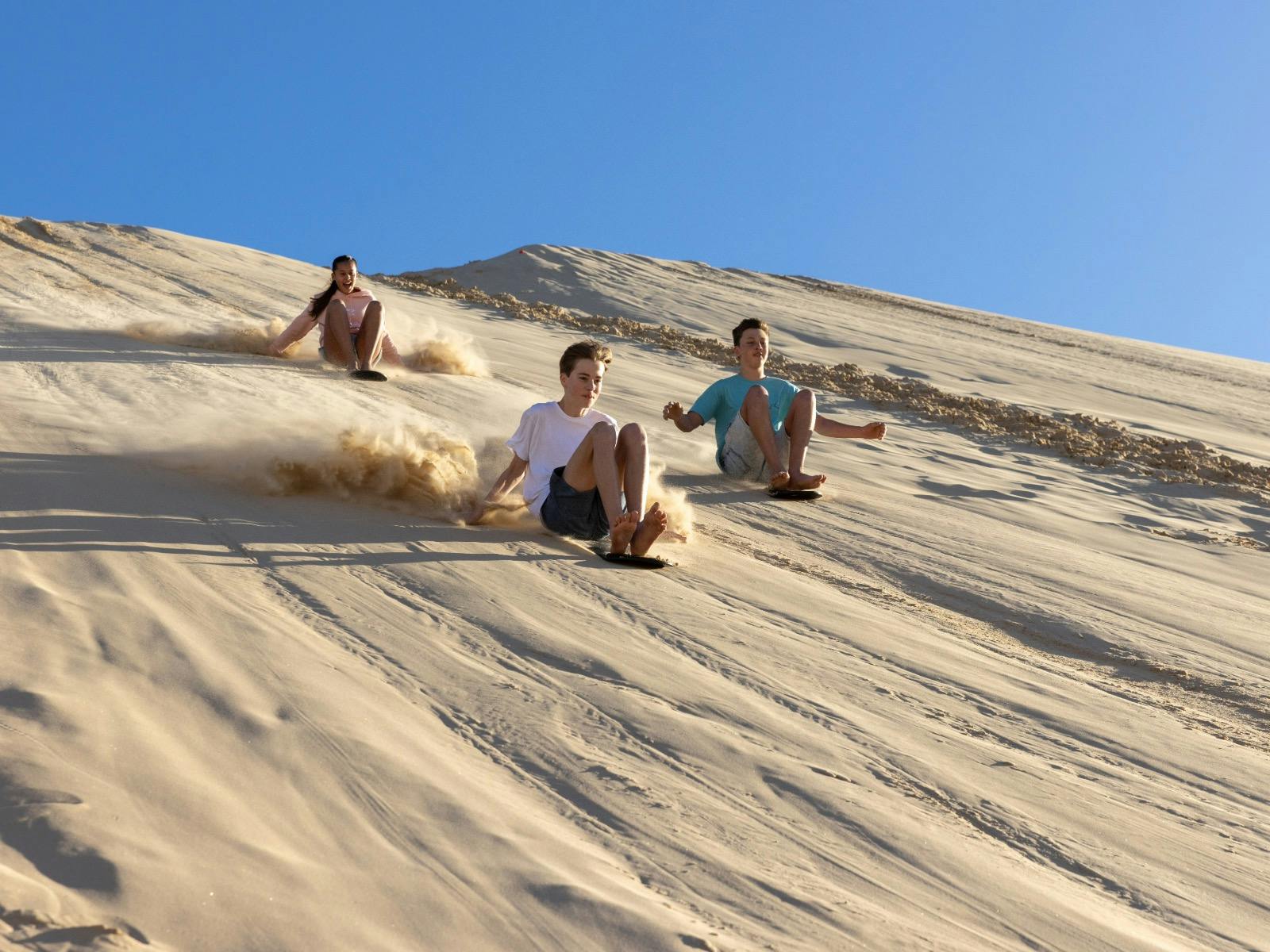 three children sliding down the sand dune