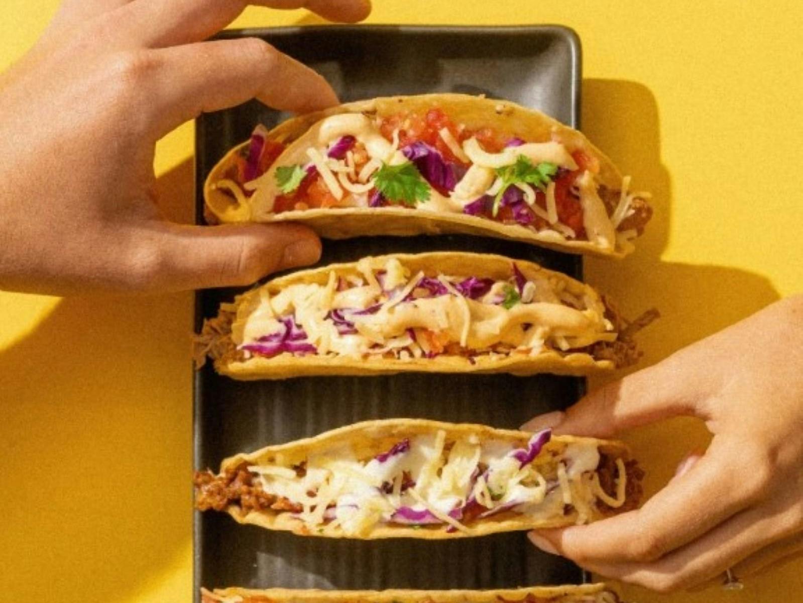 Hands grabbing tacos from yellow table