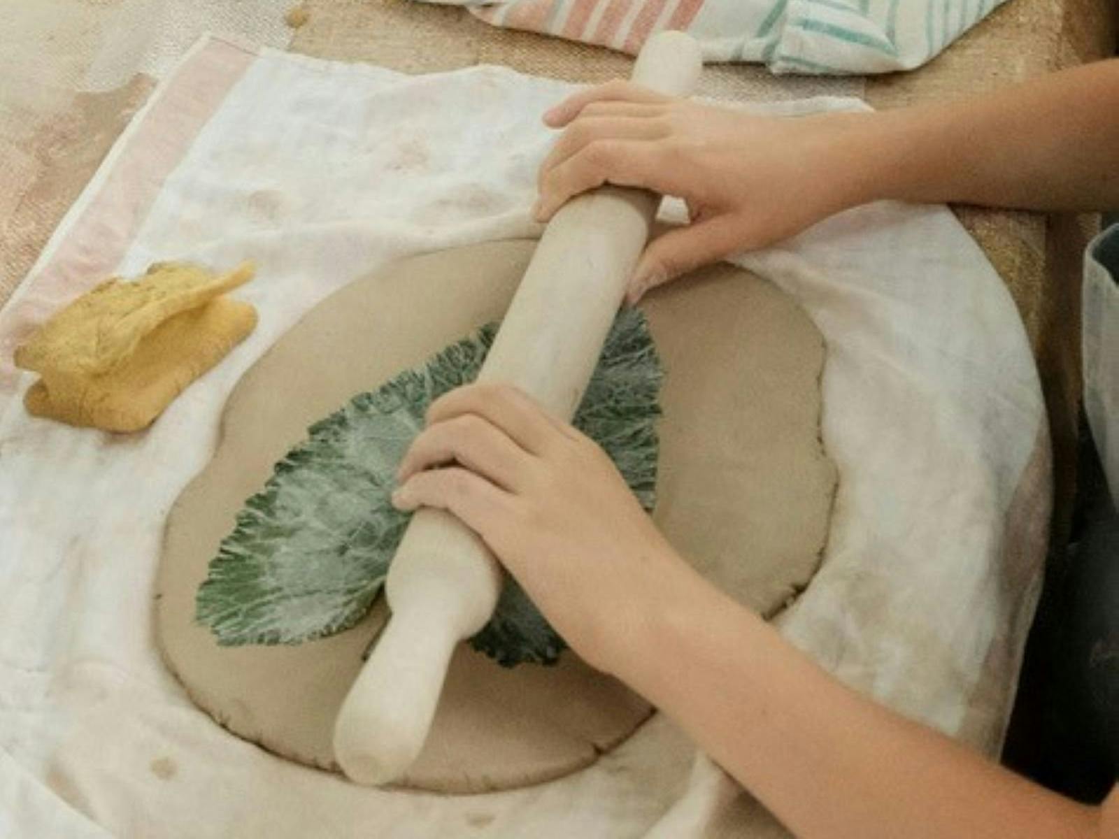 Hands rolling our pottery with a leaf imprint