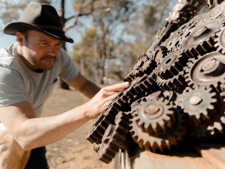 A man touches a rusted metal sculpture of a ram.