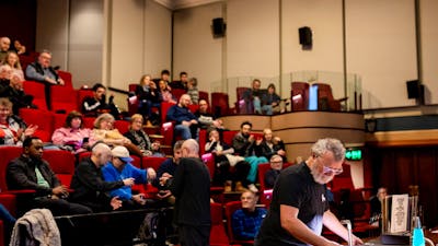 Audience in a theatre and a man at the front preparing to play a vinyl
