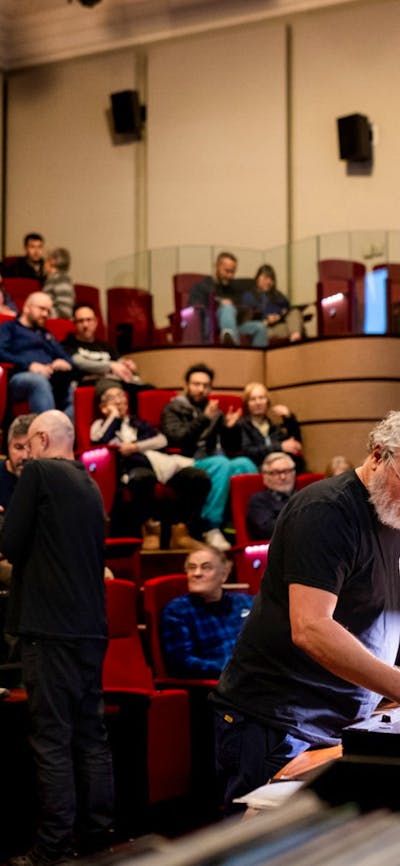 Audience in a theatre and a man at the front preparing to play a vinyl