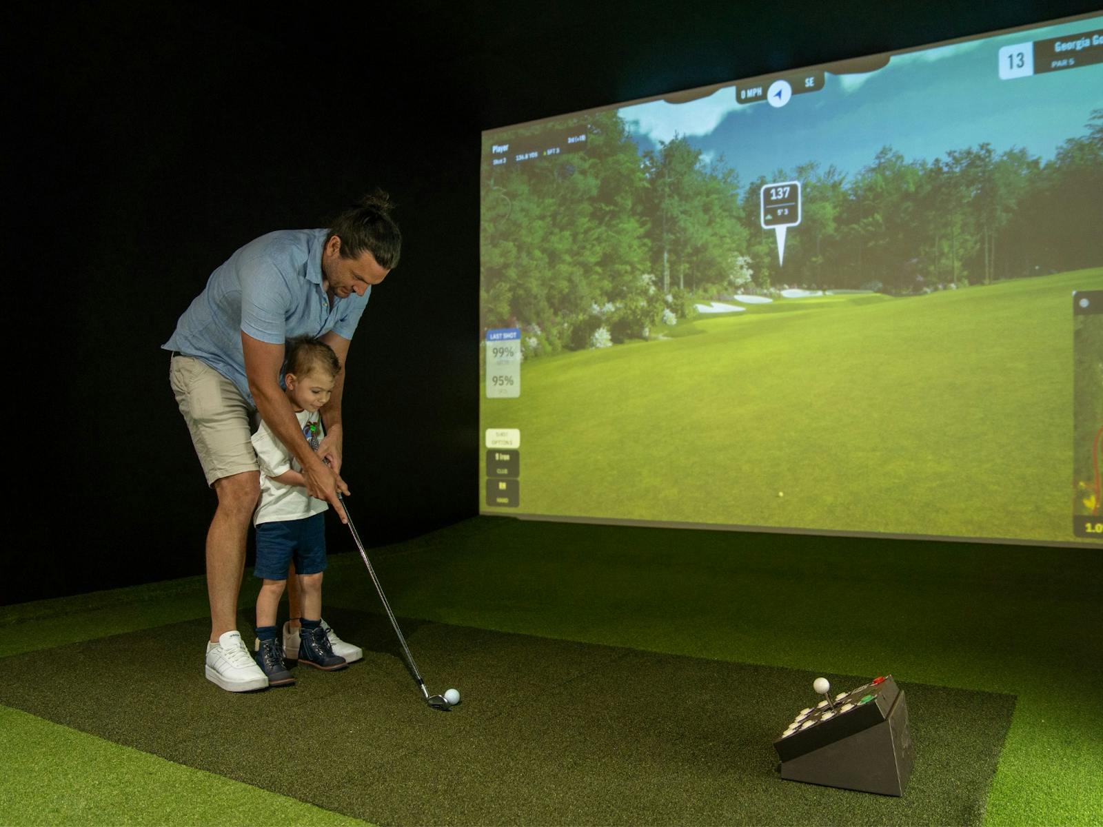 A father teaches his young son how to putt using the golf simulator A father teaches his young son how to putt using the golf simulator