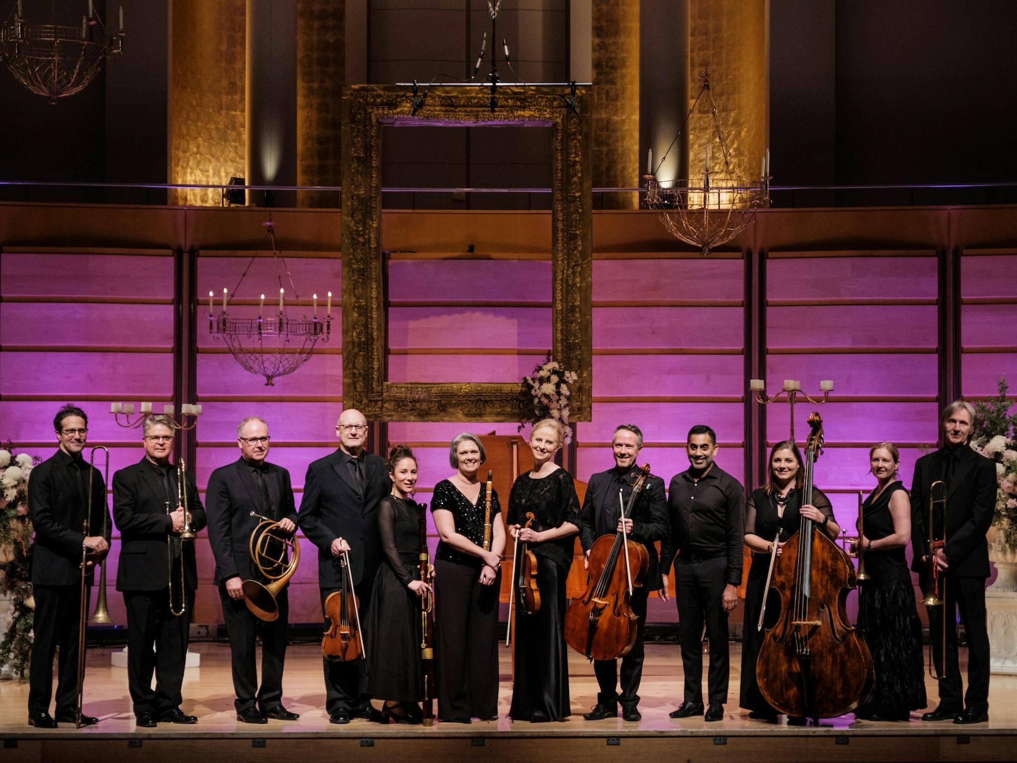 Orchestra standing onstage with period instruments.