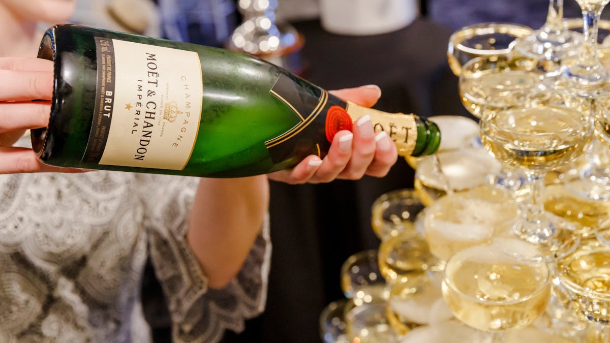 A smiling woman pouting Moet into a glass on a champagne tower