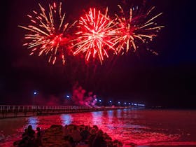 A photo of orangey red fireworks pointing outwards, lighting up the sky near the Beachport jetty.