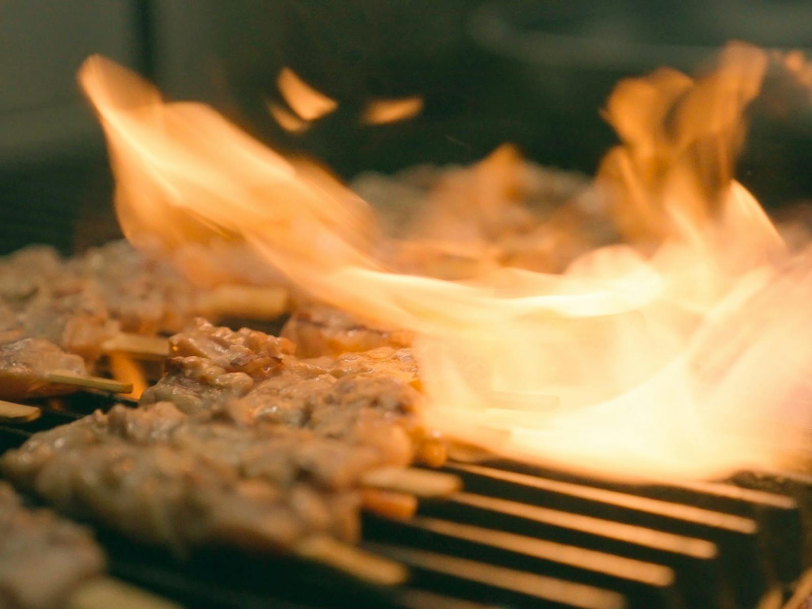 chicken schewers being cooked on the grill plate with flame in the background