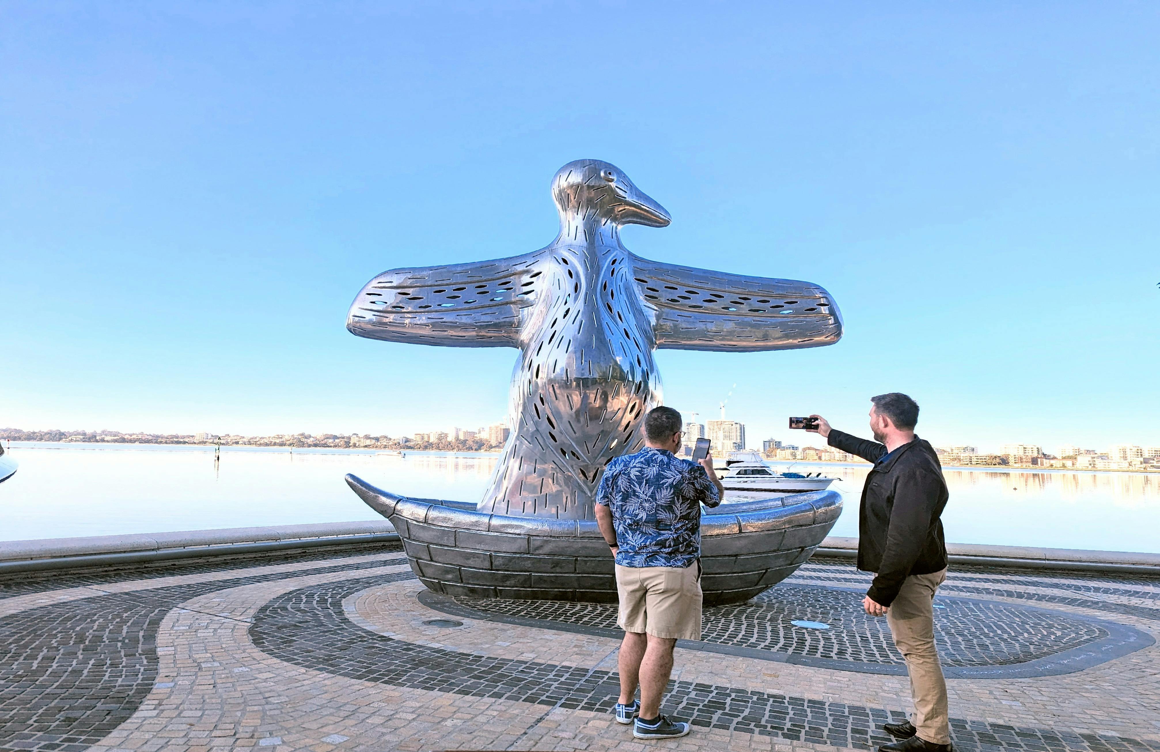 Two men take photos of the First Contact silver bird statue