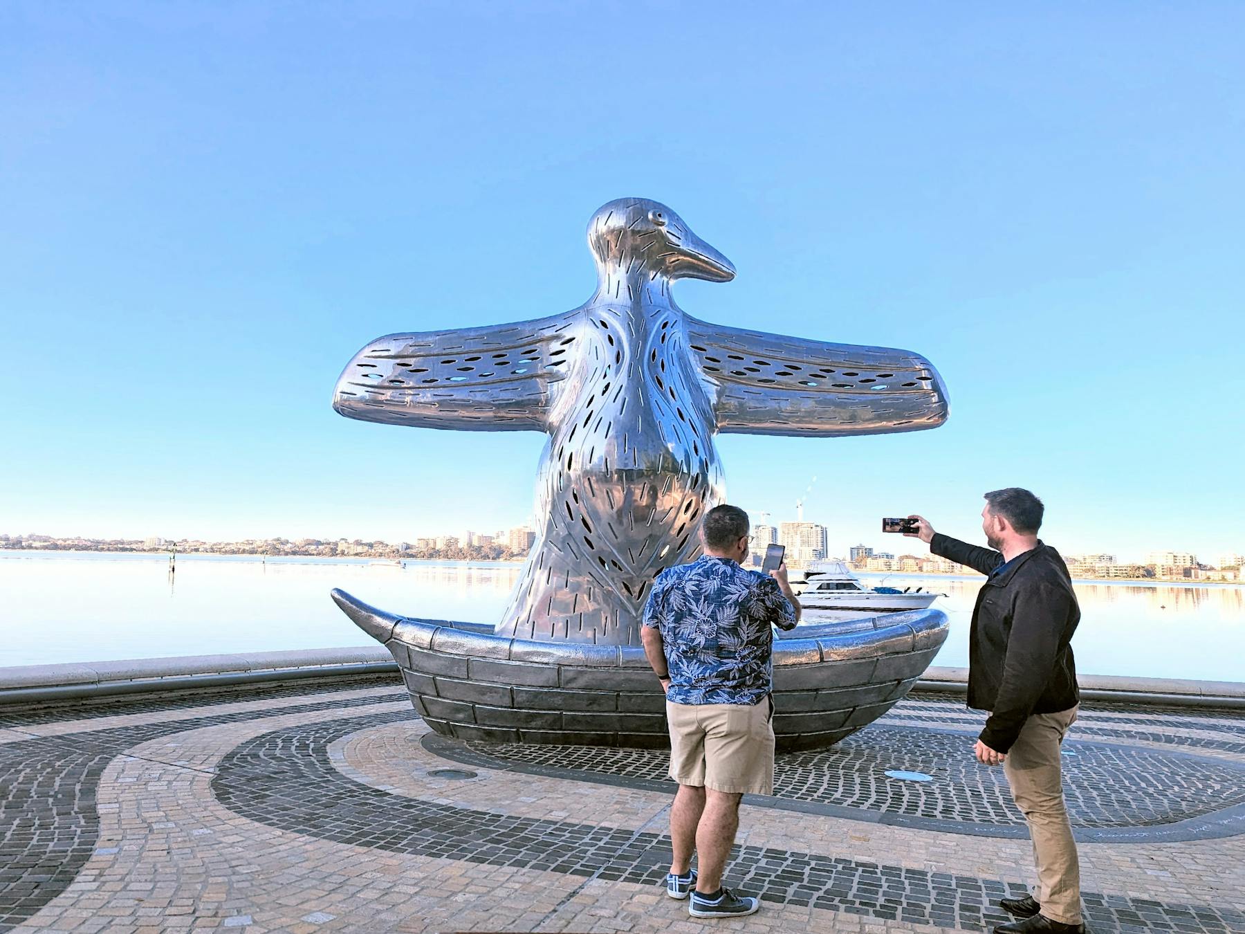 Two men take photos of the First Contact silver bird statue