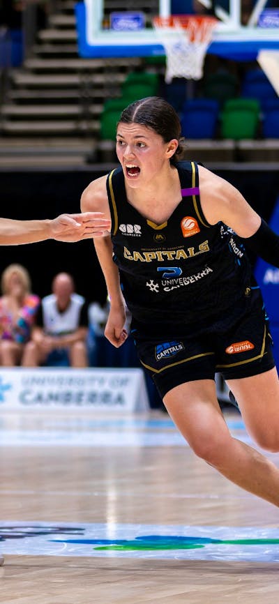 UC Capitals player driving to the basket for a layup during a WNBL game.