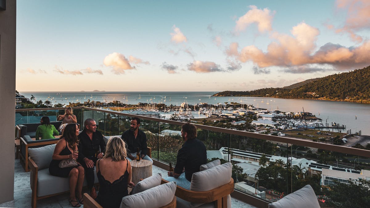 People socializing in lounge chairs on Elementa Whitsundays rooftop, overlooking the port and ocean.
