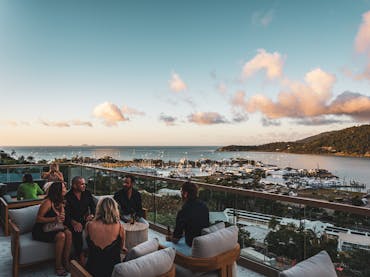 People socializing in lounge chairs on Elementa Whitsundays rooftop, overlooking the port and ocean.