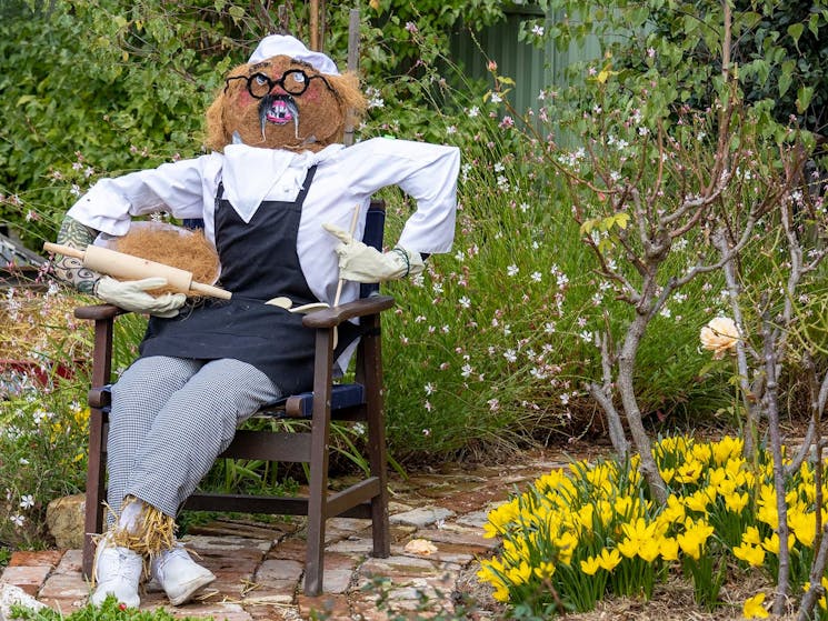 a scarecros dressed as a baker lounging on a chair with rolling pin