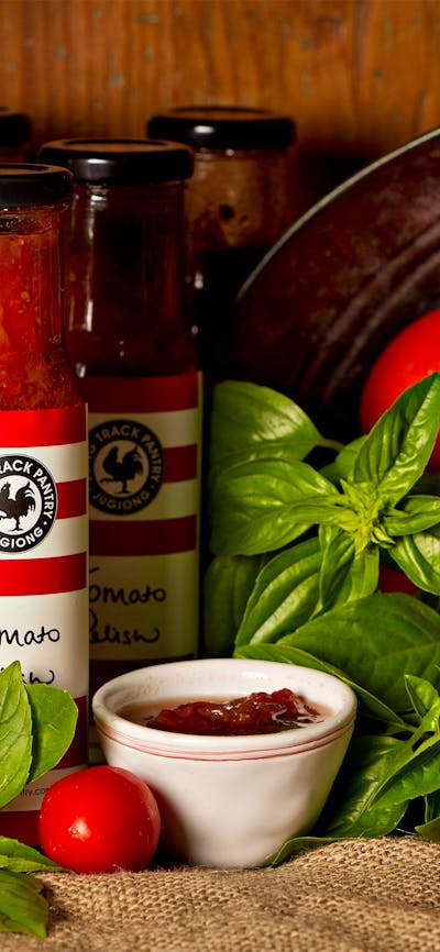 Jars of homemade relishes with fresh tomatoes and basil