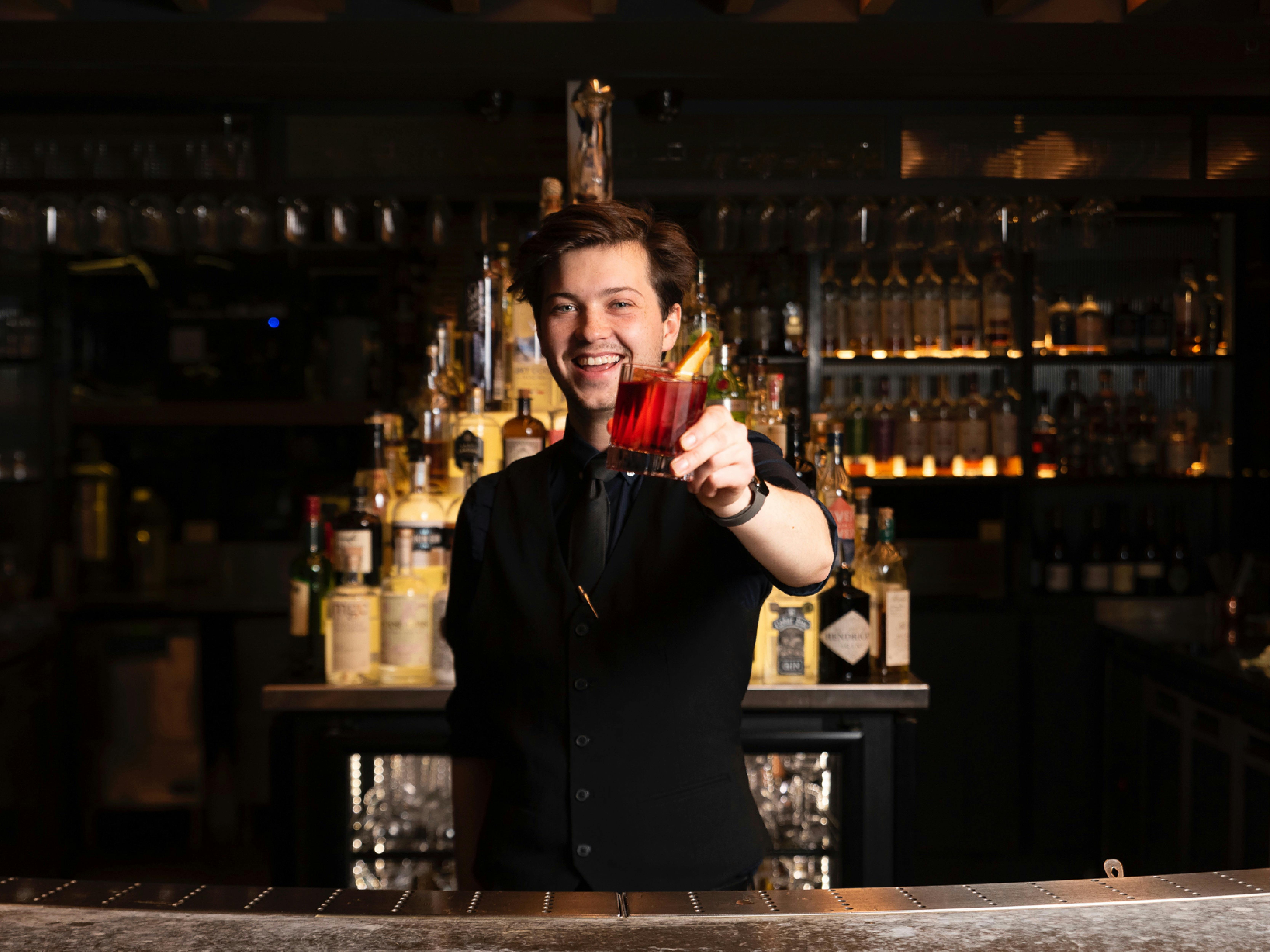 Cocktail bar with a bartender presenting a red cocktail