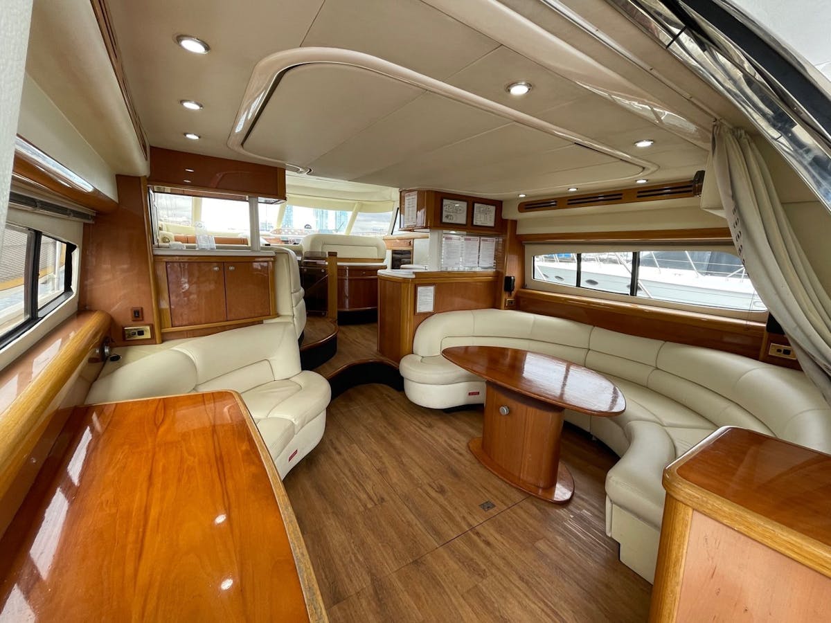 Luxury yacht interior showing curved leather lounge seating, dining table, and polished timber cabin Luxury yacht interior showing curved leather lounge seating, dining table, and polished timber cabin