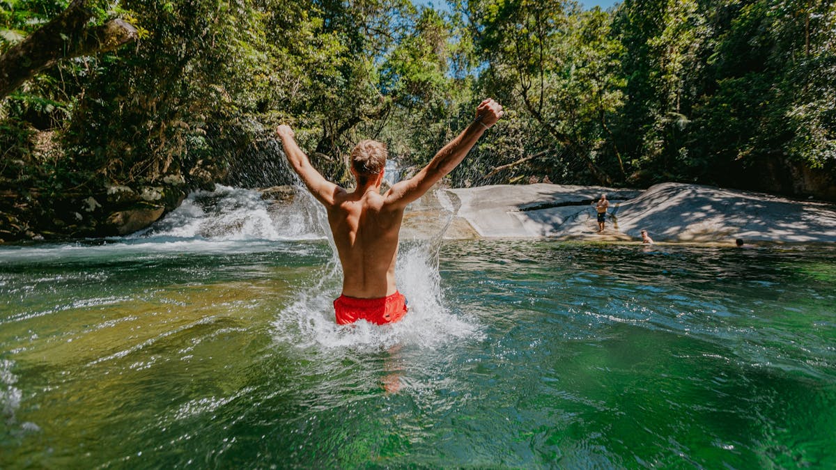 Male with his back turned to camera with is arms extended out in celebration at Josephine Falls